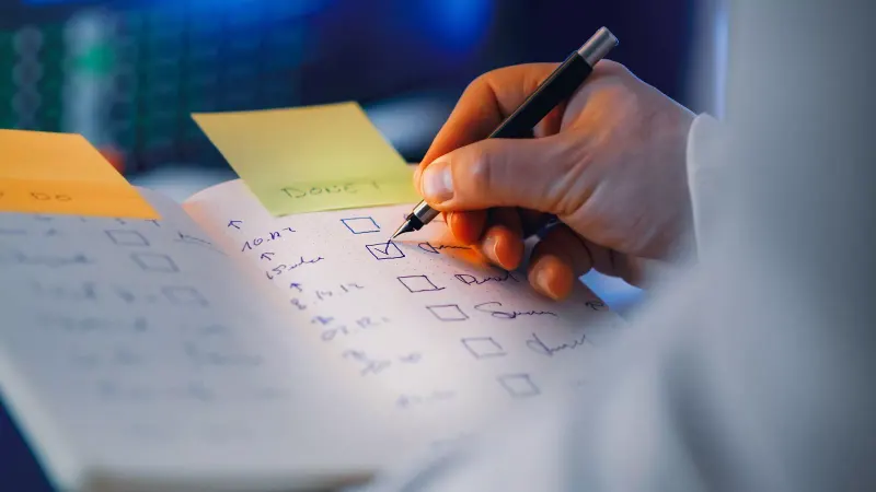 Close-up of a hand writing in a notebook with checkboxes, highlighting productivity and organization.