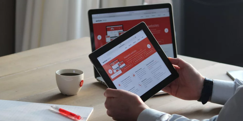 Business professional using a tablet and laptop with a hot drink, focusing on digital content review.