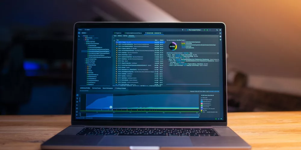 A laptop displaying code on a wooden desk, in a dimly lit workspace.