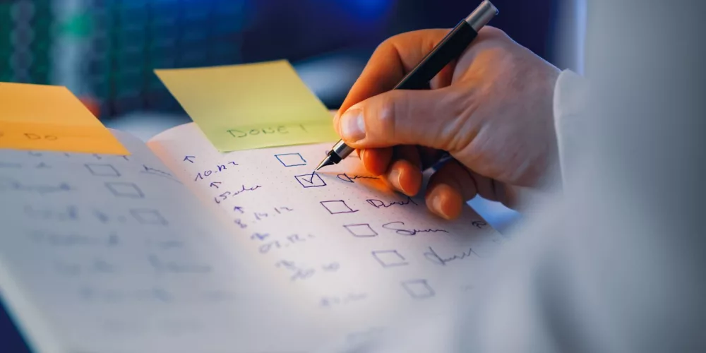 Close-up of a hand writing in a notebook with checkboxes, highlighting productivity and organization.